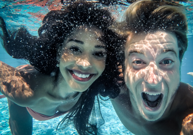 junges Paar lacht in die Kamera unter Wasser im Pool